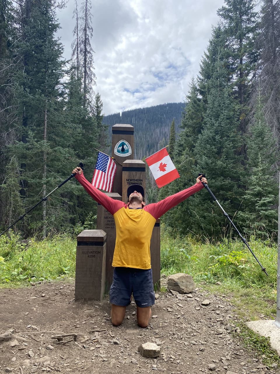 Atlas kneeling with arms and poles raised at the northern terminus of the PCT